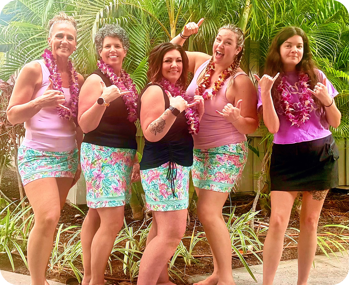 Five women in tropical outfits, smiling together.