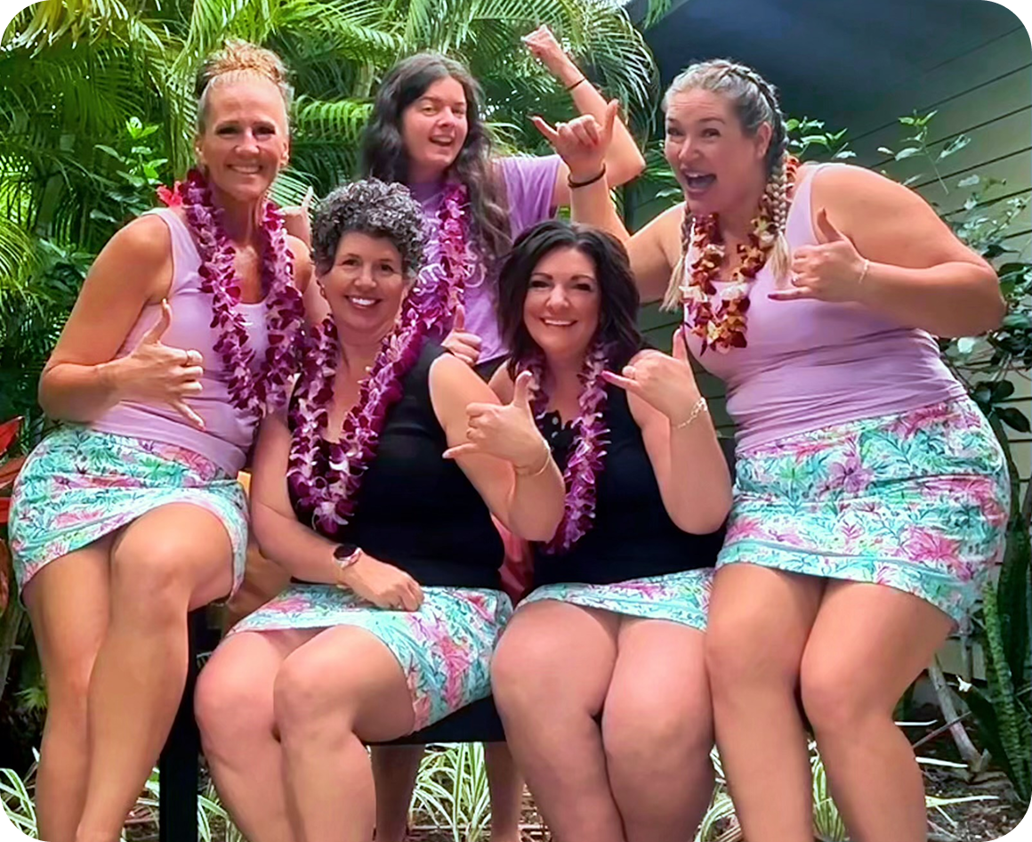 Five women wearing leis, smiling and posing.
