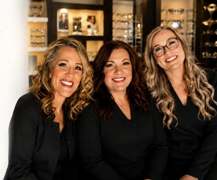 Three women sitting at a table in front of a display case filled with glasses
